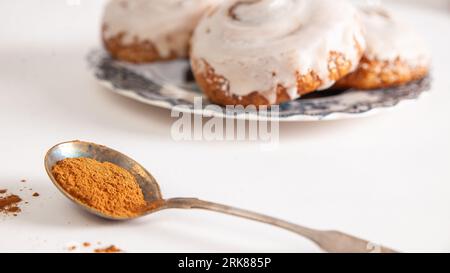 Une image en gros plan de deux rouleaux de cannelle Cinnabon sur des assiettes, avec une cuillère de cannelle en poudre sur le côté Banque D'Images