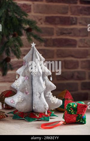 Arbre de Noël en tissu argenté entouré de jouets décoratifs souples pour arbre de Noël sur fond de mur de briques Banque D'Images