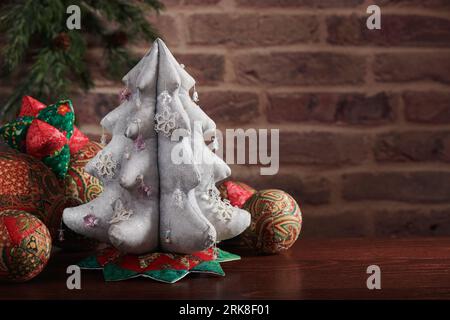 Arbre de Noël en tissu argenté entouré de jouets décoratifs souples pour arbre de Noël sur fond de mur de briques Banque D'Images