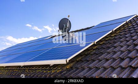 Système photovoltaïque privé avec panneaux solaires sur le toit d'une maison avec tuiles groupées autour d'une antenne parabolique Banque D'Images