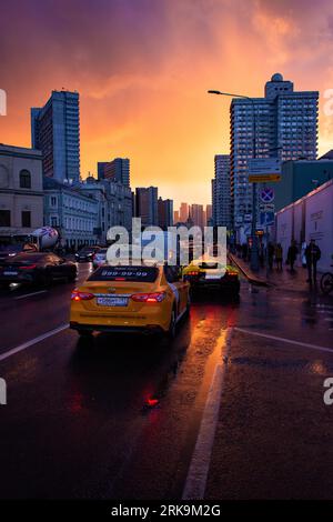 La rue Arbat de Moscou prend vie sous un ciel envoûtant de coucher de soleil, ses bâtiments soviétiques historiques et la circulation animée se prélassant dans la lueur post-pluie. Banque D'Images