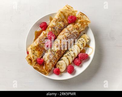 crêpes fraîchement cuites décorées avec framboises, banane et sauce caramel sur assiette blanche, vue de dessus Banque D'Images