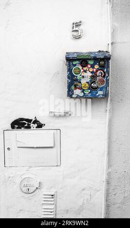 Lagos, Algarve, Portugal- 23 octobre 2022 : boîte aux lettres en métal bleu pleine d'autocollants à côté de graffitis dormant de chat Banque D'Images