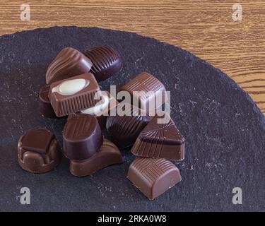 Une délicieuse variété de chocolat mise en valeur sur un plateau en ardoise, posé sur une table en bois pâle pour une touche gourmande Banque D'Images