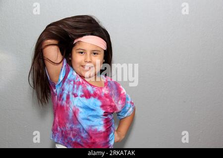 Fille hispanique de 10 ans avec de très longs cheveux noirs droits modelant heureusement pour la caméra dans une chemise de style cravate dye Banque D'Images