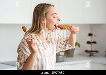 Jeune femme mangeant du pain grillé avec du beurre de noix dans la cuisine Banque D'Images