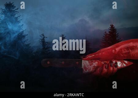 Main avec couteau taché de sang dans la forêt sombre Banque D'Images
