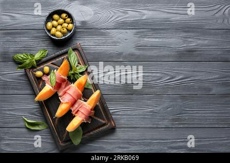 Savoureux melon avec prosciutto, basilic et olives vertes sur fond de bois foncé Banque D'Images