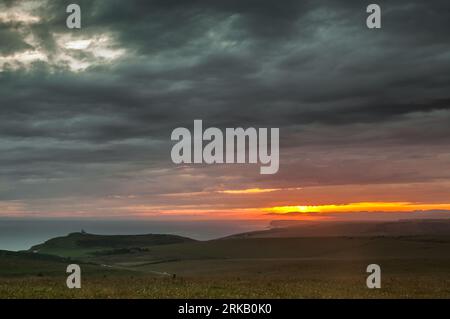 Beachy Head, Eastbourne, Sussex, Royaume-Uni. 24 août 2023. Bref aperçu du coucher du soleil sous les nuages orageux tandis que la brume de mer pénètre. Photo prise depuis la région de Beachy Head, vue vers l'ouest, au-dessus des falaises de Birling Gap et Seven Sisters. Phare Belle tout à gauche de la photo. Crédit : David Burr/Alamy Live News Banque D'Images