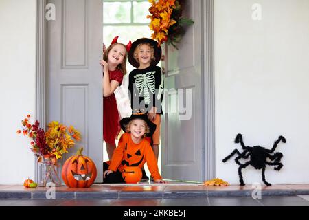 Les enfants trichent ou gâtent le soir d'Halloween. Les enfants habillés à la porte de la maison décorée. Garçon et fille en costume de sorcière et de vampire et chapeau Banque D'Images