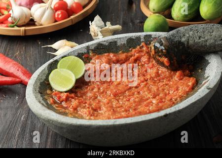 Tomate sambal ou pâte de tomate épicée sur mortier de pierre et pilon, moulin traditionnel indonésien. Frais. Banque D'Images