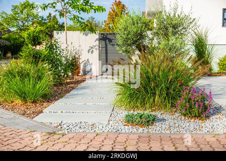 Le frontyard d'une maison moderne, détails de jardin avec des plantes colorées, lits d'herbe sèche entourés de rochers gris. Banque D'Images