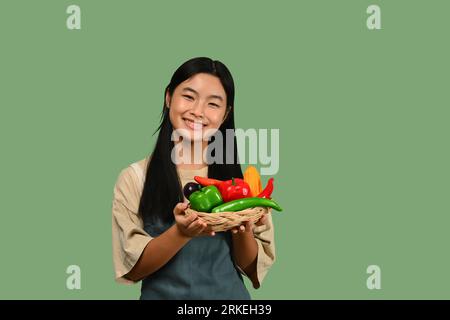 Jolie adolescente asiatique tenant le panier avec des légumes isolés sur fond vert. Concept de nourriture saine Banque D'Images