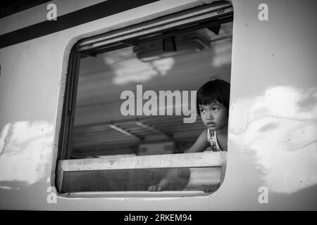 Bangkok, Thaïlande - 6 mars 2020 : photo en noir et blanc d'une jeune fille asiatique, jetant un coup d'œil par la fenêtre d'un train avant le départ. Banque D'Images