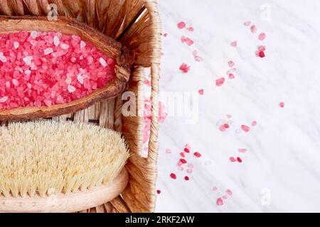 Panier de paille avec le bain et le spa équipé, camomille, brosse à récurer sur la surface en marbre. Sel marin rose. Copier l'espace pour le texte Banque D'Images