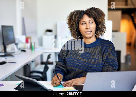 Femme d'affaires réfléchie avec des notes adhésives sur le bureau debout dans le bureau Banque D'Images