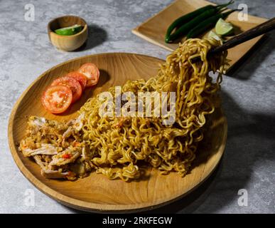 Mie goreng ayam geprek. Nouilles frites servies sur une assiette en bois accompagnées de poulet, tomates fraîches et saupoudrées d'oignons frits Banque D'Images