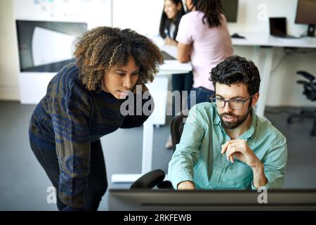 Vue à angle élevé de l'homme d'affaires confiant expliquant à la femme d'affaires sur l'ordinateur de bureau dans le bureau Banque D'Images