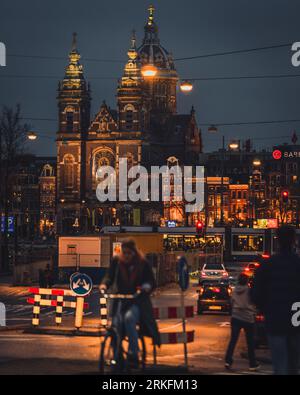 Amsterdam, pays-Bas - novembre 27 2022 : la basilique Saint-Nicolas la nuit. Un cycliste et un tramway passent devant Centraal Station, en face du Banque D'Images