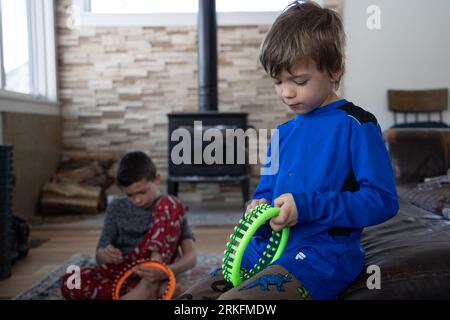 Petit garçon apprenant à tricoter assis dans le salon avec frère Banque D'Images