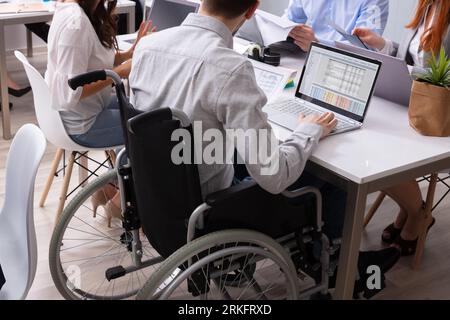 Vue latérale d'une mobilité Businessman Sitting on Wheelchair Using Laptop In Office Banque D'Images
