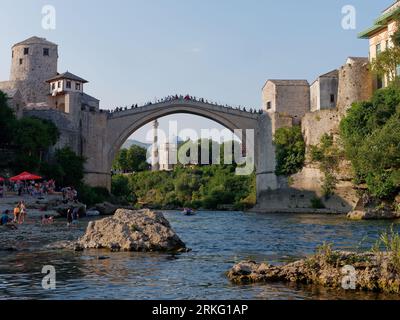 Plage à côté de la rivière Neretva et les touristes sur Stari Most (vieux pont) et Koski-Mehmed Pacha Mosquée. Mostar, Bosnie-Herzégovine, 20 août 2023. Banque D'Images