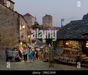 Les touristes marchent dans une rue pavée avec des boutiques de souvenirs dans la vieille ville de Mostar un soir d'été, Bosnie-Herzégovine, 20 août 2023. Banque D'Images