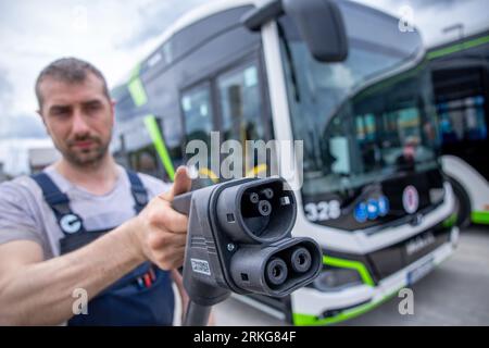 Rostock, Allemagne. 02 août 2023. Sebastian Schuh tient une prise de charge pour recharger un bus électrique au nouveau dépôt de Rostocker Straßenbahn AG (RSAG). Après six mois de travaux de conversion, le site des autobus réguliers a été adapté pour les systèmes de propulsion alternatifs. Les bus peuvent être alimentés avec de l’énergie électrique et du biométhane, et le plan est de convertir progressivement tous les services d’autobus en systèmes d’entraînement respectueux du climat au cours des prochaines années. Crédit : Jens Büttner/dpa/Alamy Live News Banque D'Images