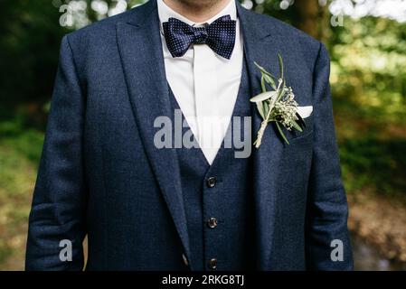 Un jeune homme à l'air confiant dans un costume bleu vif et un noeud papillon se tient les mains dans ses poches Banque D'Images