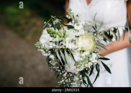 Une jeune femme portant une robe de mariée blanche se tient devant un fond blanc, berçant un bouquet de fleurs blanches dans ses bras Banque D'Images
