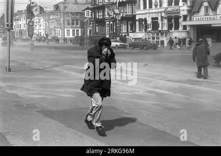 Golden Mile Blackpool 1970s Royaume-Uni. Un vent fort souffle du sable sec sur la plage et sur la promenade du Golden Mile. Un homme cache son visage dans son manteau contre les particules de sable soufflées par le vent piquant. Blackpool, Lancashire, Angleterre vers août 1970. HOMER SYKES Banque D'Images