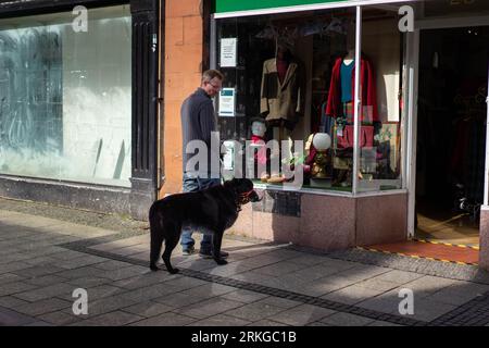 Un chien heureux de taille moyenne se tient devant un magasin avec son propriétaire Banque D'Images