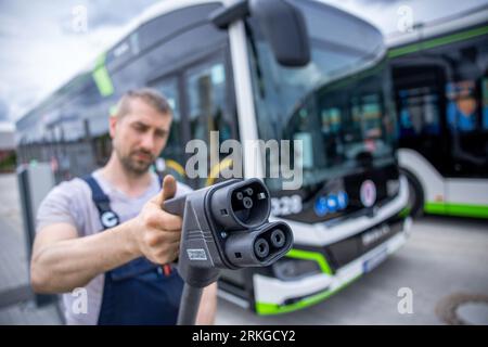 Rostock, Allemagne. 02 août 2023. Sebastian Schuh tient une prise de charge pour recharger un bus électrique au nouveau dépôt de Rostocker Straßenbahn AG (RSAG). Après six mois de travaux de conversion, le site des autobus réguliers a été adapté pour les systèmes de propulsion alternatifs. Les bus peuvent être alimentés avec de l’énergie électrique et du biométhane, et le plan est de convertir progressivement tous les services d’autobus en systèmes d’entraînement respectueux du climat au cours des prochaines années. Crédit : Jens Büttner/dpa/Alamy Live News Banque D'Images