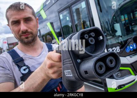 Rostock, Allemagne. 02 août 2023. Sebastian Schuh tient une prise de charge pour recharger un bus électrique au nouveau dépôt de Rostocker Straßenbahn AG (RSAG). Après six mois de travaux de conversion, le site des autobus réguliers a été adapté pour les systèmes de propulsion alternatifs. Les bus peuvent être alimentés avec de l’énergie électrique et du biométhane, et le plan est de convertir progressivement tous les services d’autobus en systèmes d’entraînement respectueux du climat au cours des prochaines années. Crédit : Jens Büttner/dpa/Alamy Live News Banque D'Images