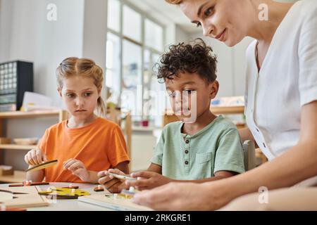 enfants interraciaux jouant avec du matériel didactique montessori près de l'enseignante féminine, diversité Banque D'Images