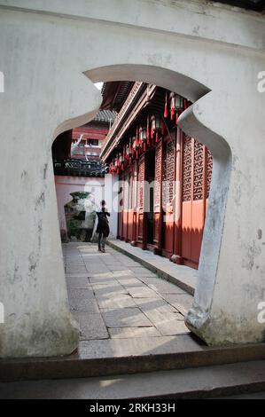 Une porte magnifique avec une jeune femme passant devant au premier plan dans le jardin Yu Yuan, Shanghai Banque D'Images