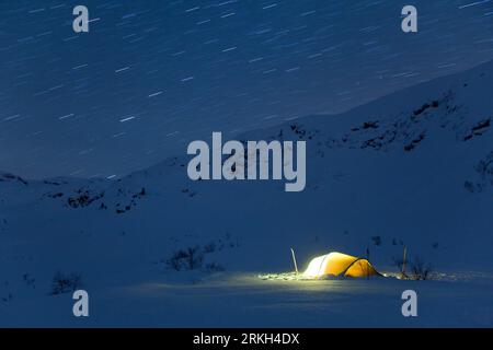 Gros plan d'une tente de camping illuminée située dans un paysage enneigé sous un ciel étoilé Banque D'Images