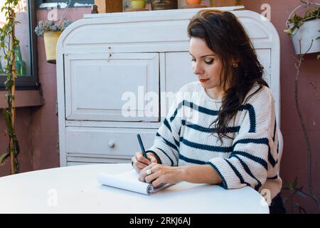 adulte française femme caucasienne graphiste est à la maison seule assise esquissant avec dessin de marqueur noir sur tampon blanc, inspiré la création de dessins pour cl Banque D'Images