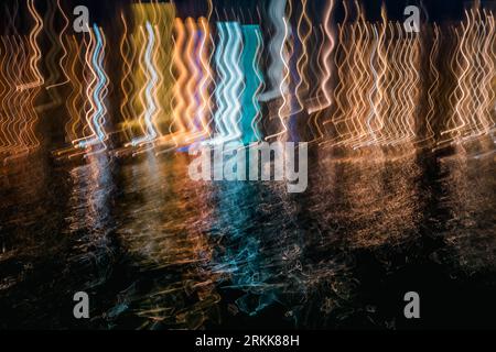 Le mouvement intentionnel de la caméra (ICM) crée des lignes ondulées à partir des lumières du restaurant et de leurs reflets dans l'eau du port vénitien de la Canée la nuit Banque D'Images