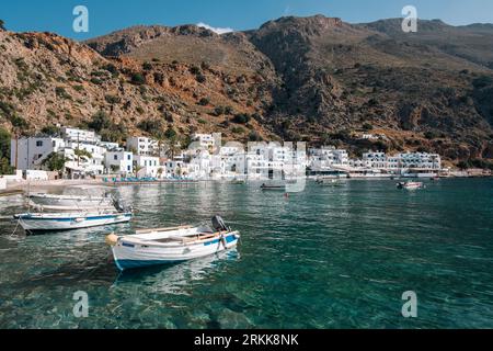 De petits bateaux flottent sur les eaux claires et émeraudes de la mer dans le pittoresque village blanchi à la chaux de Loutro, en Crète. Banque D'Images