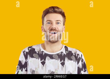Portrait d'un jeune homme barbu surpris à bouche ouverte isolé sur fond jaune studio. Banque D'Images