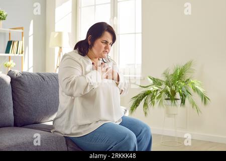 Jeune femme de poids lourd assise sur le canapé souffrant de problèmes cardiaques. Banque D'Images