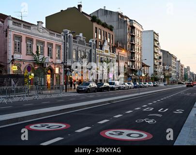Rue principale du centre-ville en début de soirée avec magasins éclairés, limite de vitesse 30, piste cyclable et bus balisée sur la route, Aveiro, Portugal Banque D'Images