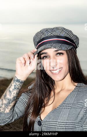 Jeune élégance urbaine : Brunette confiante dans une robe courte et chapeau, flattant tatouages expressifs Banque D'Images