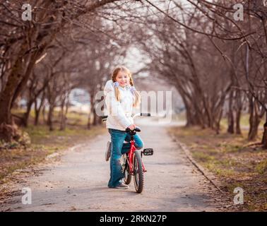 souriant petite fille heureuse debout près du vélo au printemps Banque D'Images