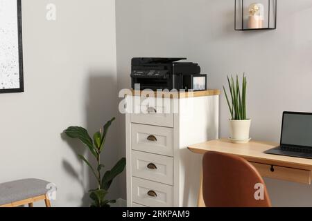 Imprimante moderne sur la commode près de la table en bois à l'intérieur Banque D'Images