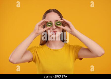 Jeune femme tenant des moitiés de kiwi près de ses yeux sur fond jaune Banque D'Images