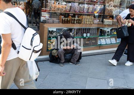 Izmir, Turquie. 25 août 2023. Un sans-abri est assis devant un magasin de noix. Il montre l'effet du temps chaud à ?zmir. Les gens sont descendus dans la rue malgré le temps chaud. Crédit : SOPA Images Limited/Alamy Live News Banque D'Images