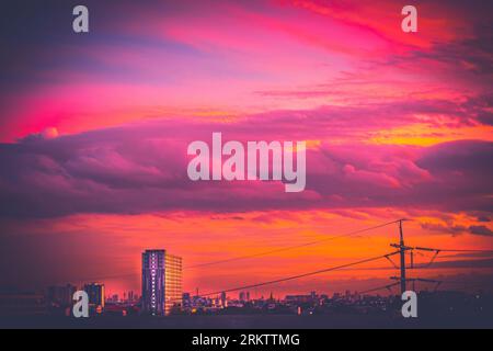 Nuages colorés de coucher de soleil affichant des teintes violettes et magenta intenses sur un bâtiment lointain de gratte-ciel et des poteaux utilitaires au crépuscule Banque D'Images