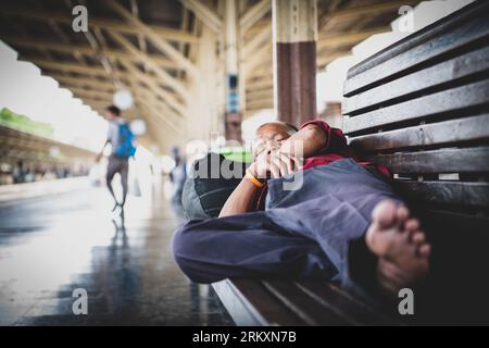 Bangkok, Thaïlande - 6 mars 2020 : un homme est capturé en train de dormir sur un banc à un quai de la gare de Bangkok, en Thaïlande. Banque D'Images